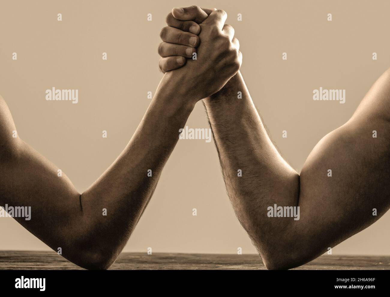 Arm wrestling. Heavily muscled man arm wrestling a puny weak man. Arms wrestling thin hand and a big strong arm in studio. Two man's hands clasped arm Stock Photo