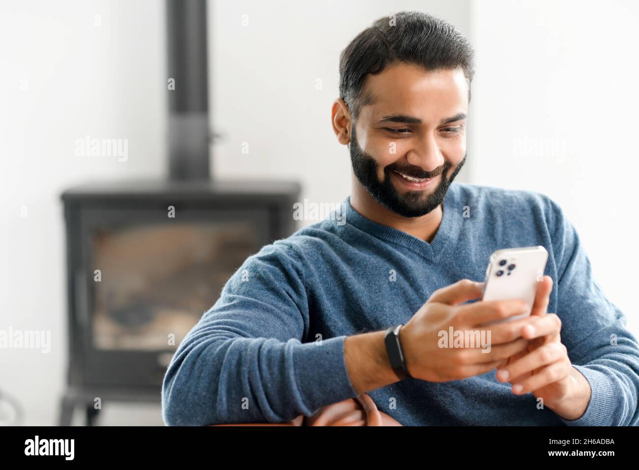 Smiling Indian guy wearing casual outfit messaging, texting on the   bearded man sits on the modern sofa and using mobile  app, scrolling feed news, websurfing, playing game Stock Photo - Alamy