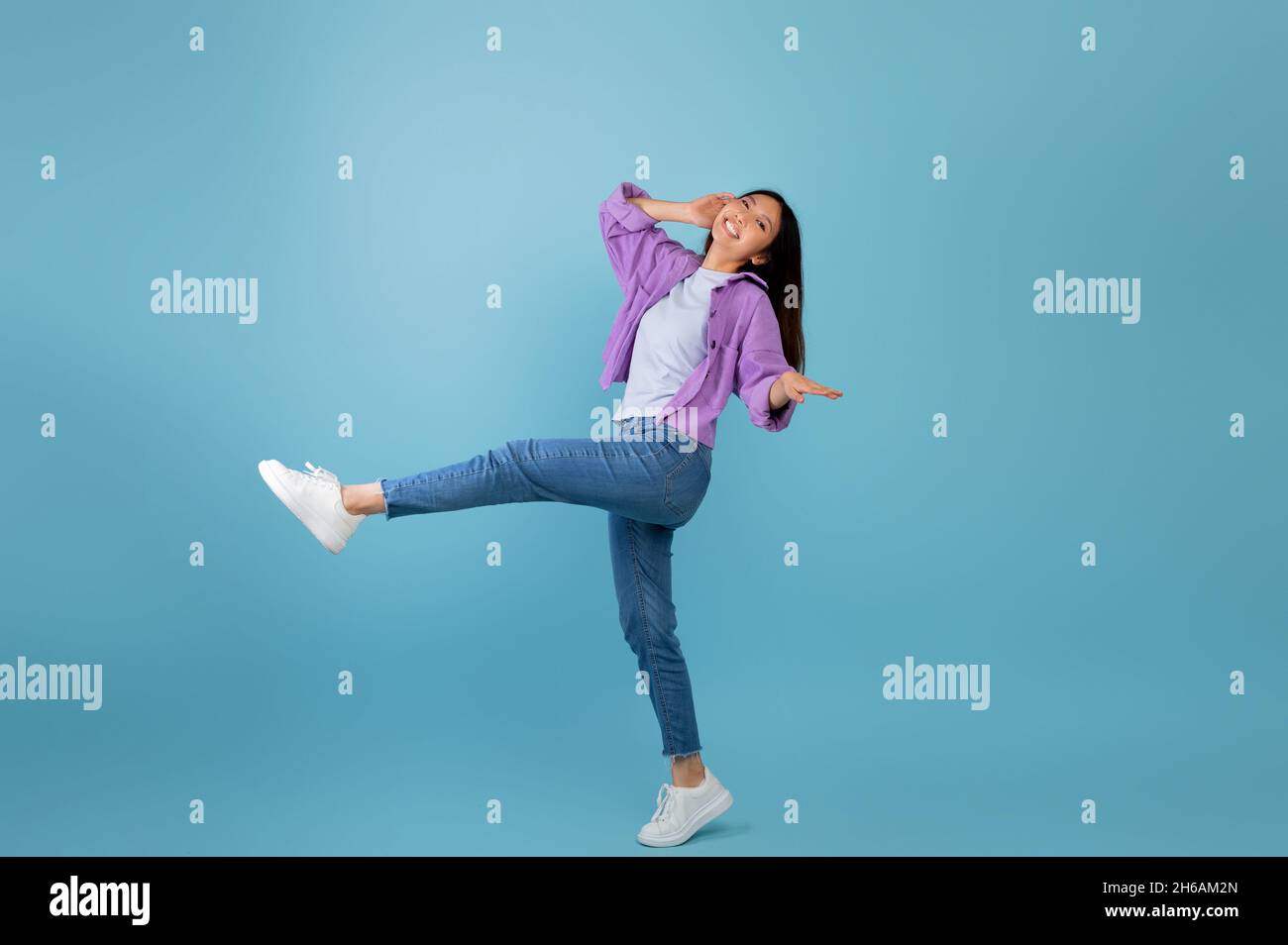 Having fun. Joyful asian lady dancing and fooling around, being in a good mood, celebrating triumph over blue studio background. Full body length shot Stock Photo