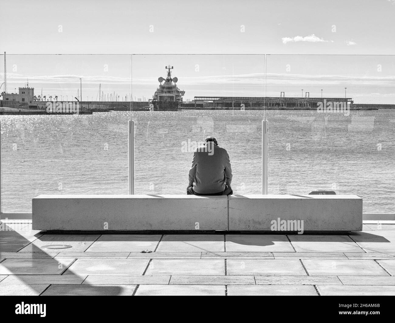 Older man sitting alone on a bench in front of the sea in the harbour Stock Photo