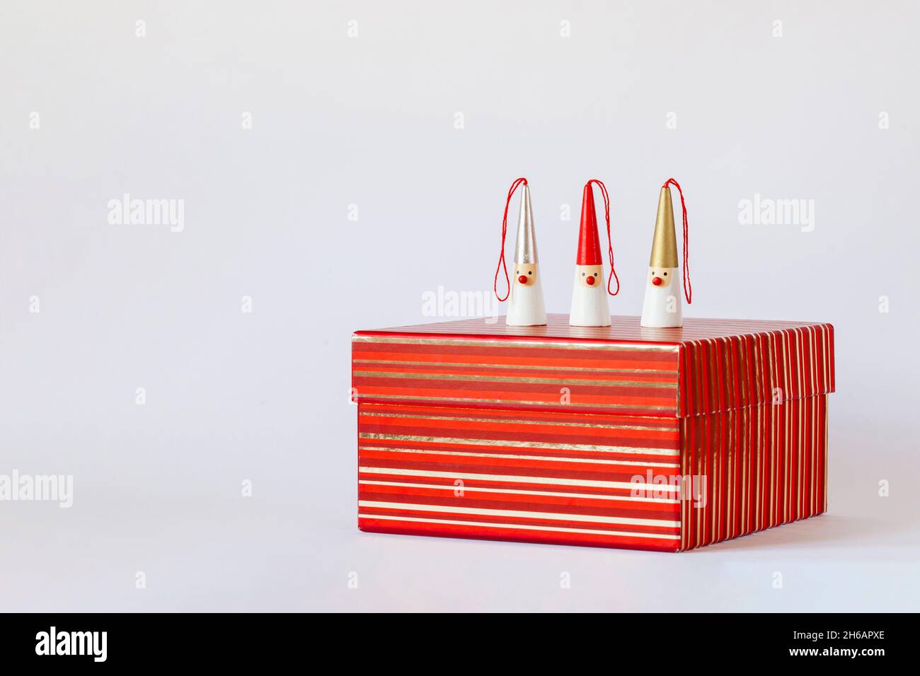 three Santa Clauses figures on a red striped gift box, white background ...