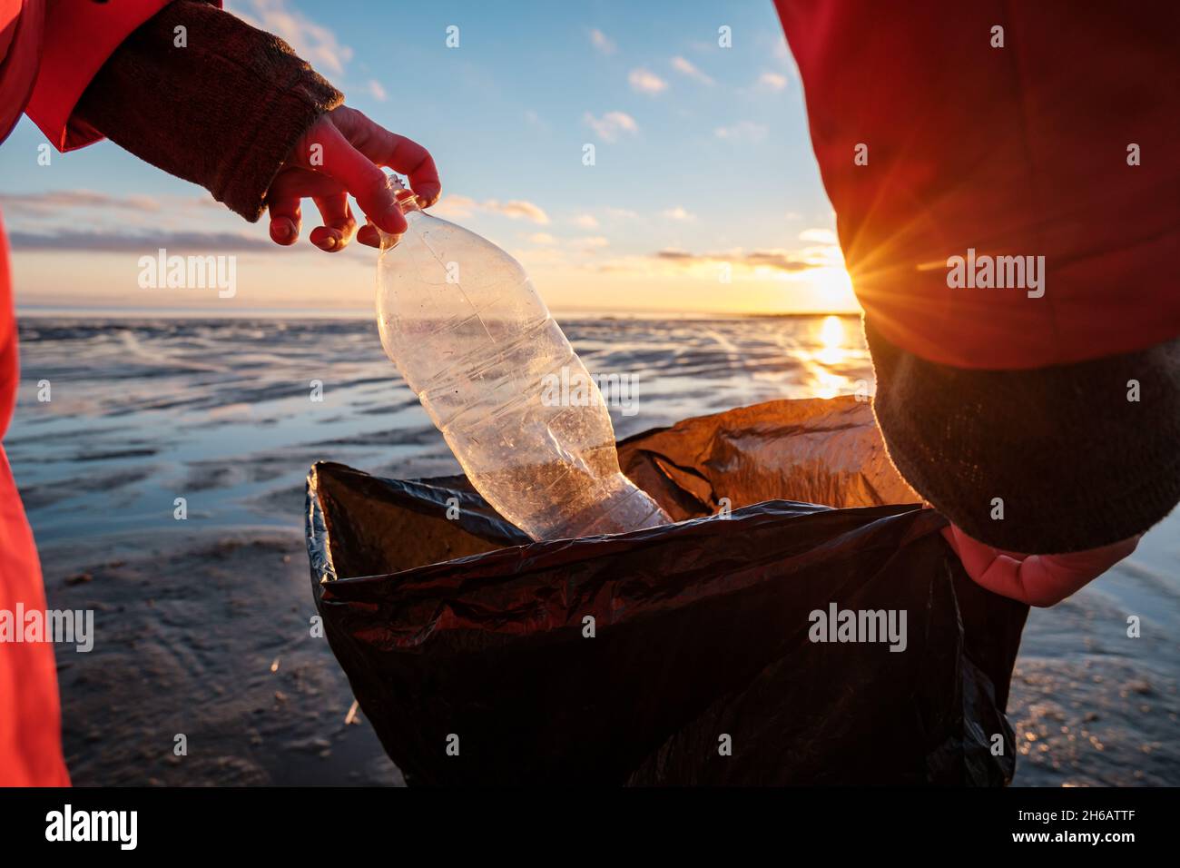 A woman cleans the bank of plastic bottles and puts the trash in a garbage bag. Environmental pollution by plastic. Recyclable packaging. Stock Photo