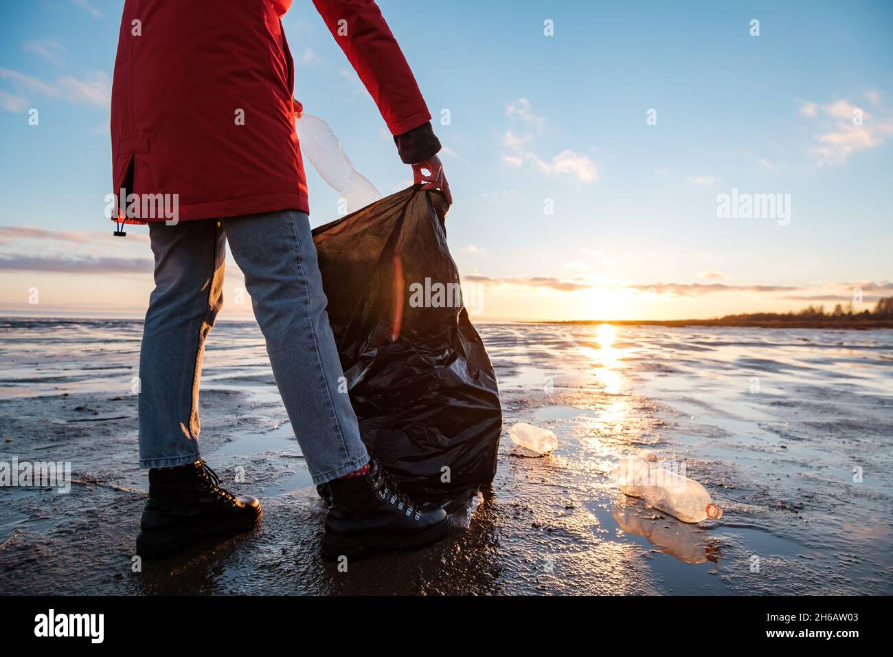 A woman cleans the bank of plastic bottles and puts the trash in a