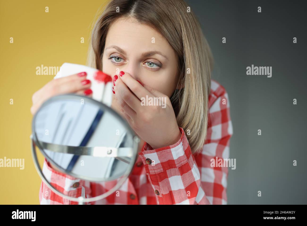 Young woman looks in mirror and bleeds from nose Stock Photo