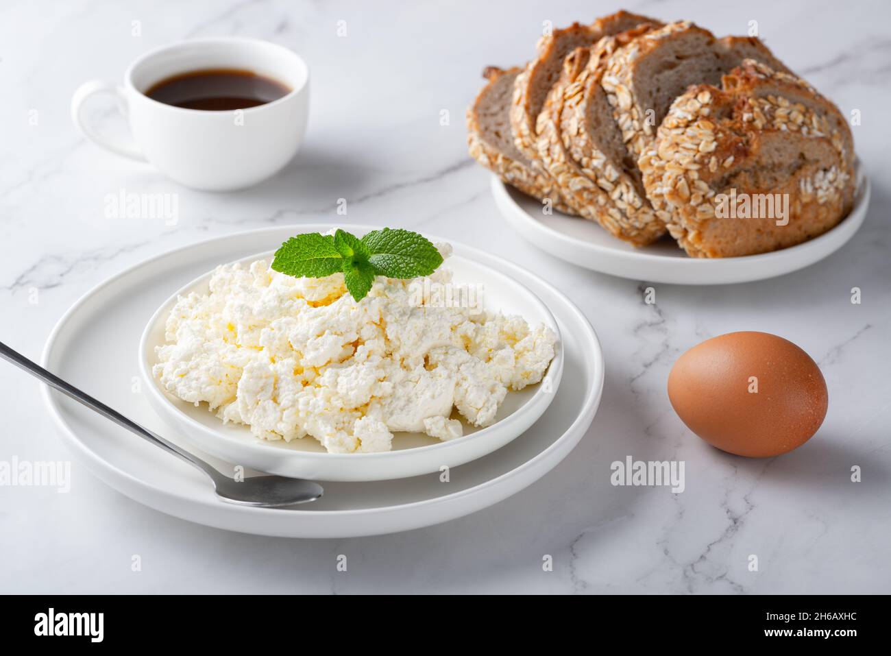 A bowl with fresh cottage cheese, rye bread and coffee on the table. Stock Photo