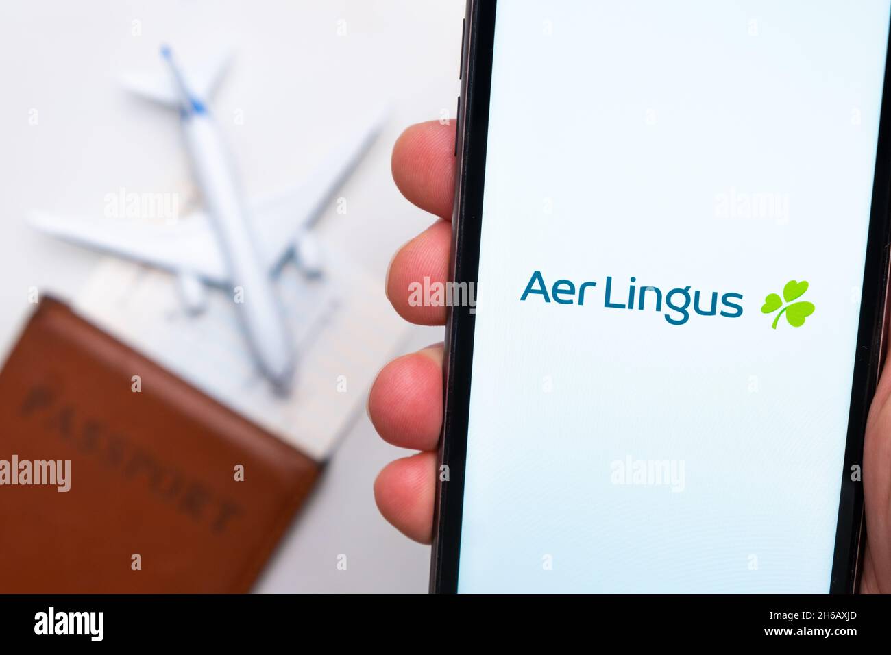 Aer Lingus Airline application on the smartphone screen mans hand. A white toy airplane and a passport are lying on a table with a light surface.November 2021, San Francisco, USA Stock Photo