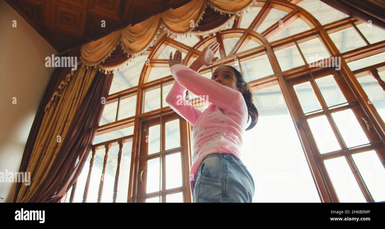 A low angle shot of a little Indian girl dancing next to the window