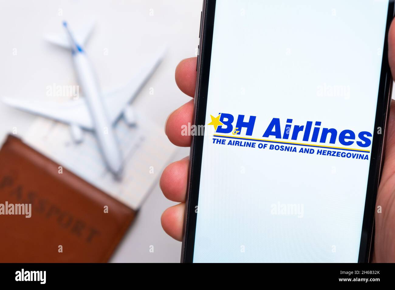 BH Airlines airline. A mobile phone and BH Airlines application in mans hand. There is a passport and a plane on a white table. November 2021, San Francisco, USA Stock Photo