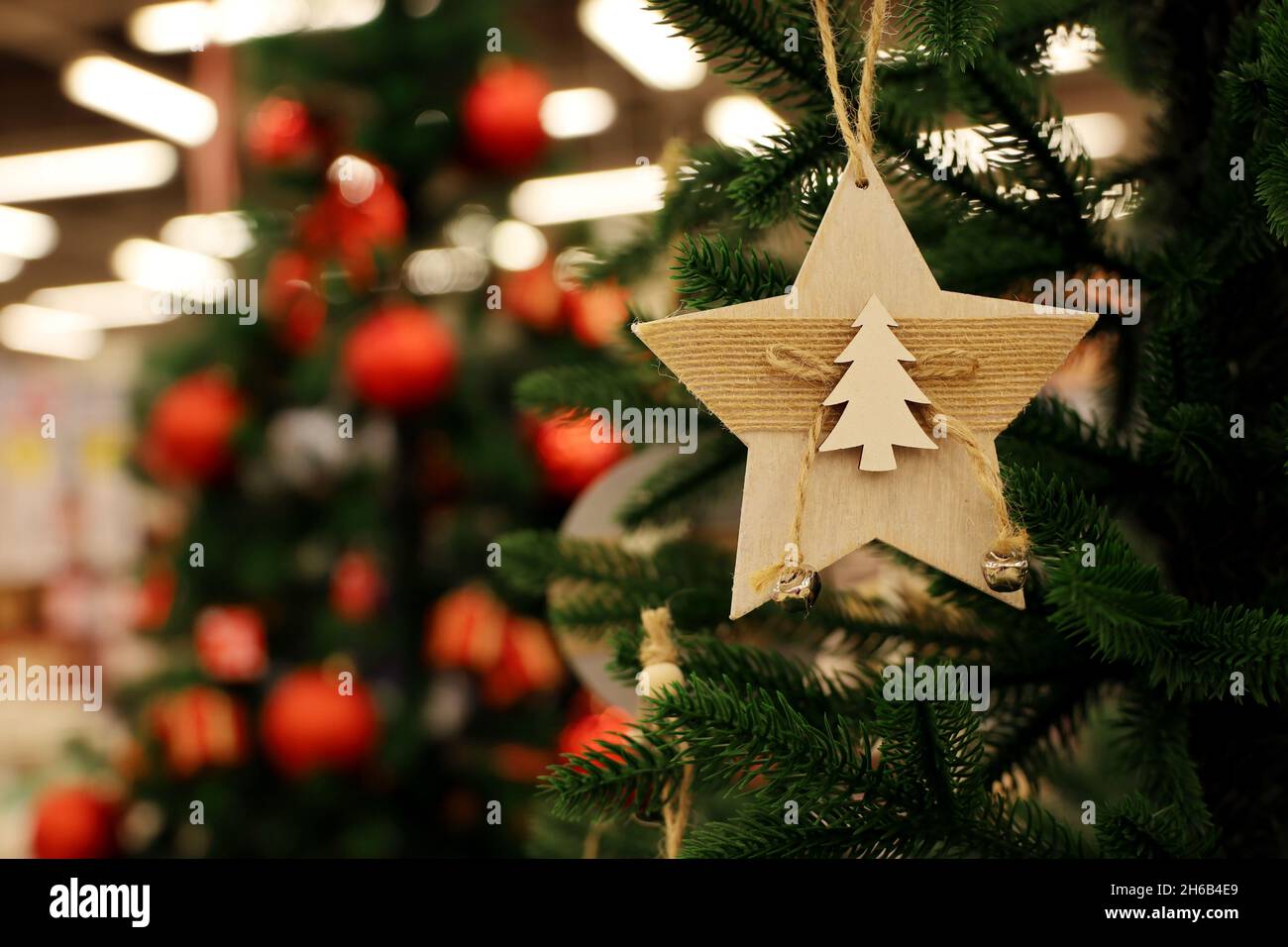 Christmas tree with decorations on blurred lights background. Wooden toy in star shape on a branch, New Year celebration Stock Photo
