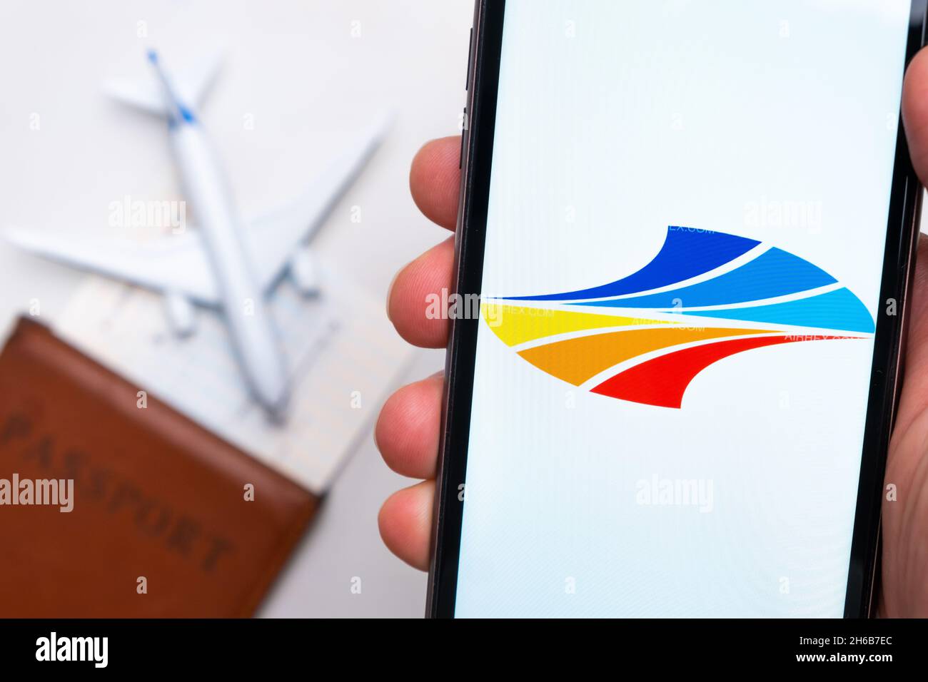 BH Air airline. A mobile phone and flybe airline application in mans hand. There is a passport and a plane on a white table. November 2021, San Francisco, USA Stock Photo
