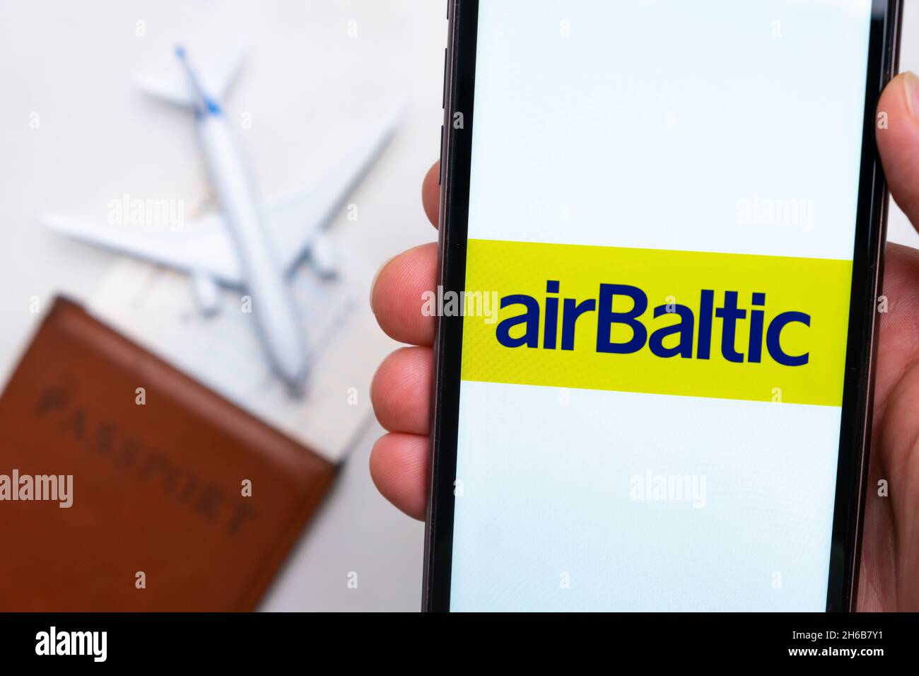 AirBaltic Airline application on the smartphone screen mans hand. A white toy airplane and a passport are lying on a table with a light surface.November 2021, San Francisco, USA Stock Photo