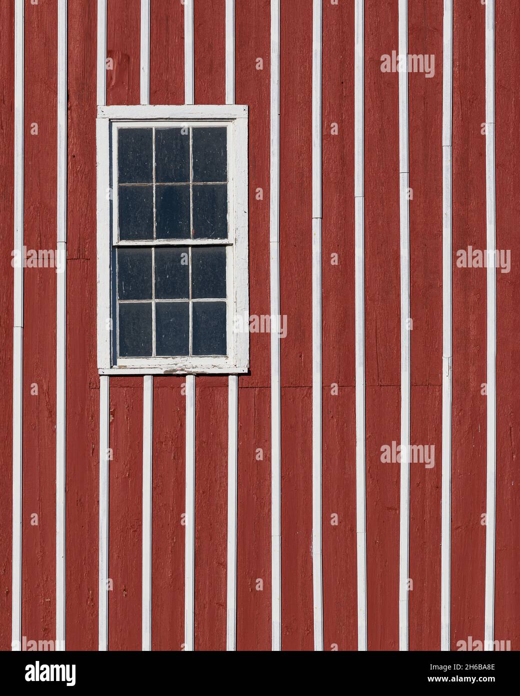 Window on red and white striped wooden exterior wall of a barn Stock Photo