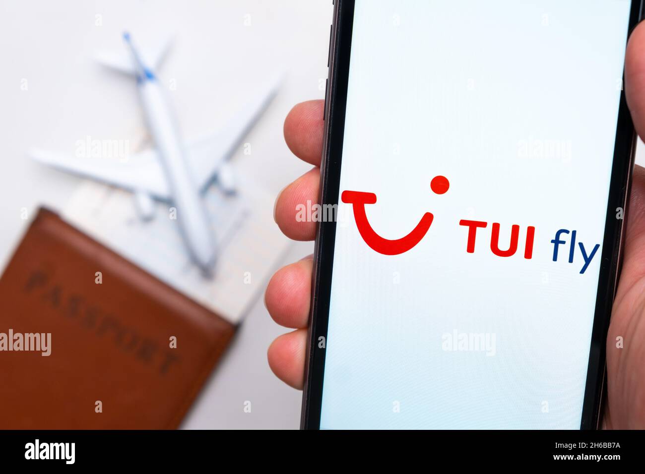 Tui fly airline. A mobile phone and Tui fly airline application in mans hand. There is a passport and a plane on a white table. November 2021, San Francisco, USA Stock Photo
