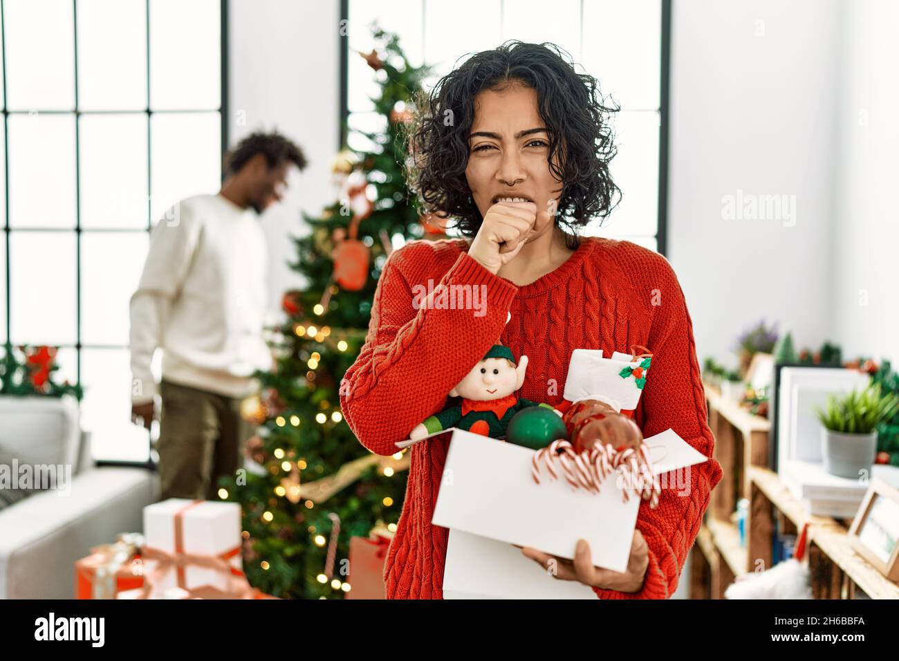 Young hispanic woman standing by christmas tree with decoration feeling