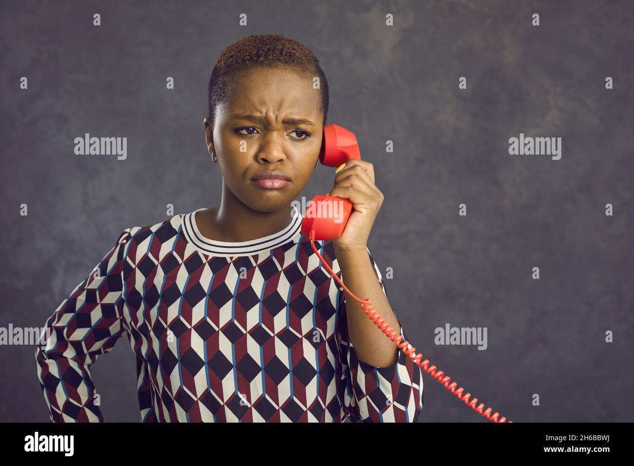Portrait of sad dark-skinned woman who was upset while talking on landline retro phone. Stock Photo