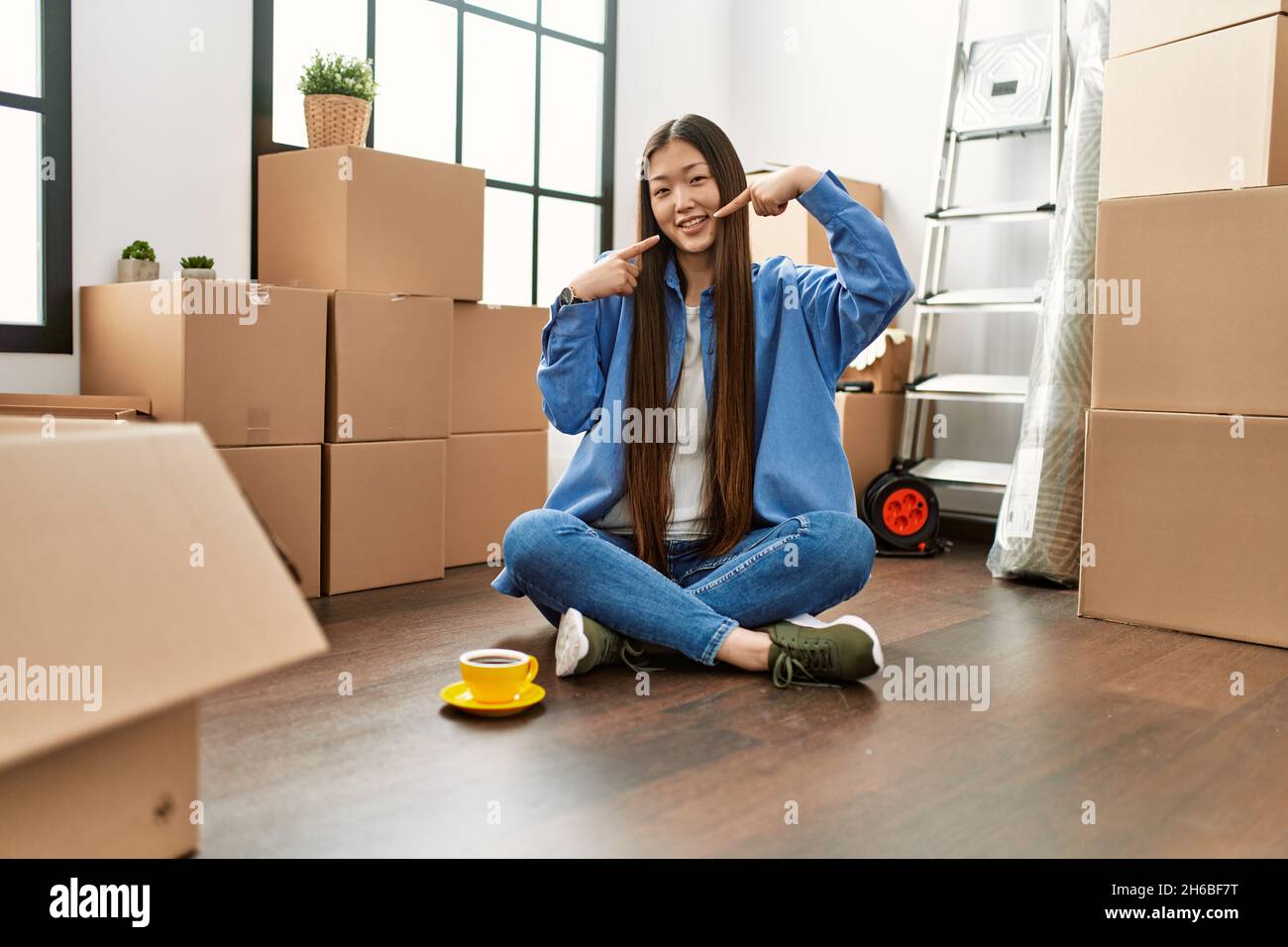 Young chinese girl sitting on the floor at new home smiling cheerful ...