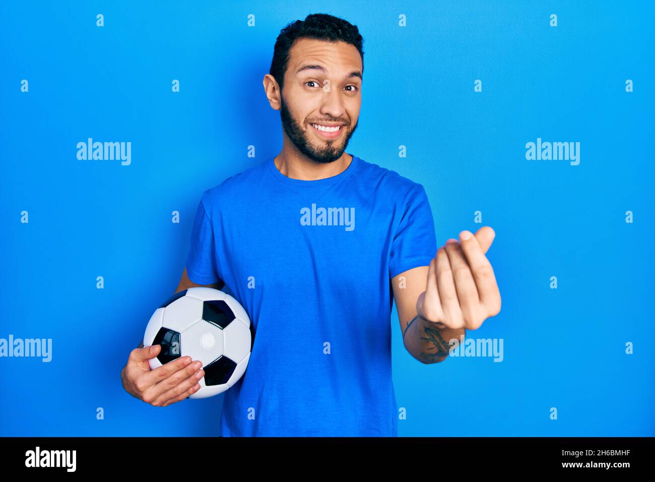Hispanic man with beard holding soccer ball doing money gesture with