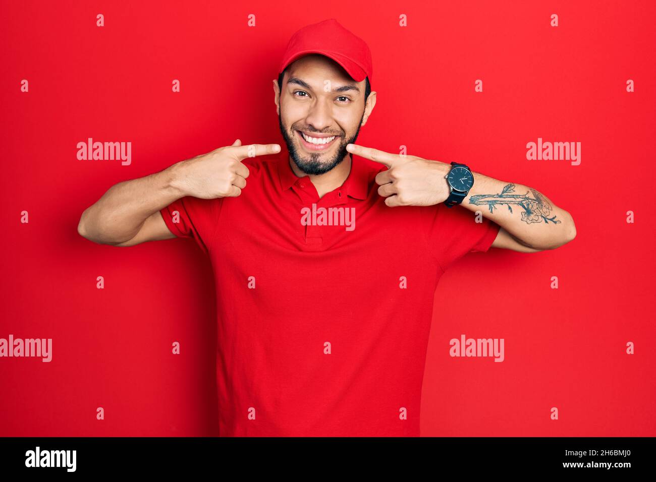 Hispanic man with beard wearing delivery uniform and cap smiling