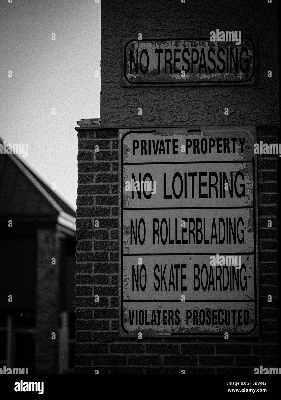 A grayscale of trespassing signes of ''No Loitering'', 'No Rollerblading', 'No Skate Boarding' on the side of a brick wall Stock Photo