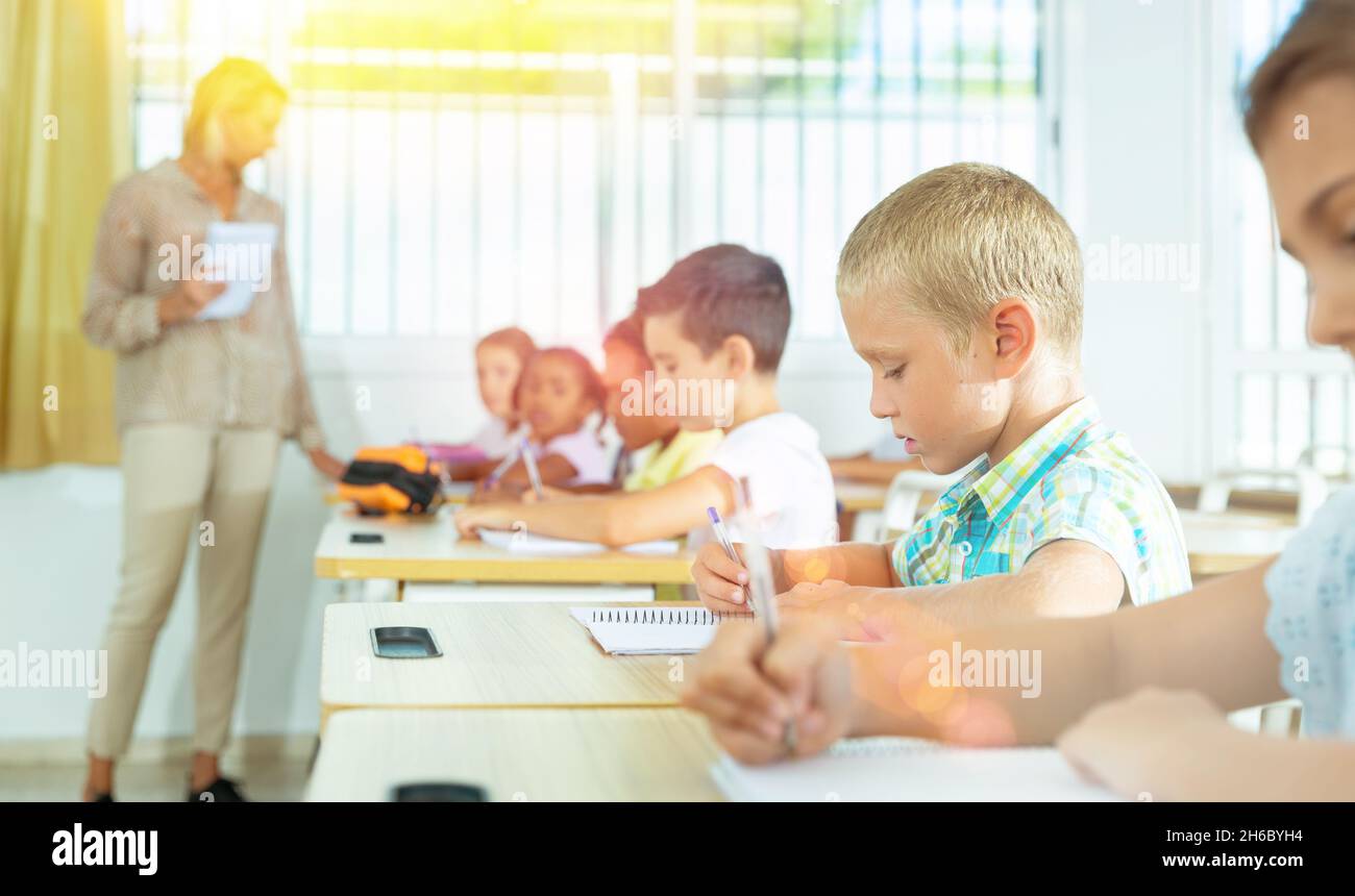 Focused tween boy writing exercises in classroom during lesson Stock Photo