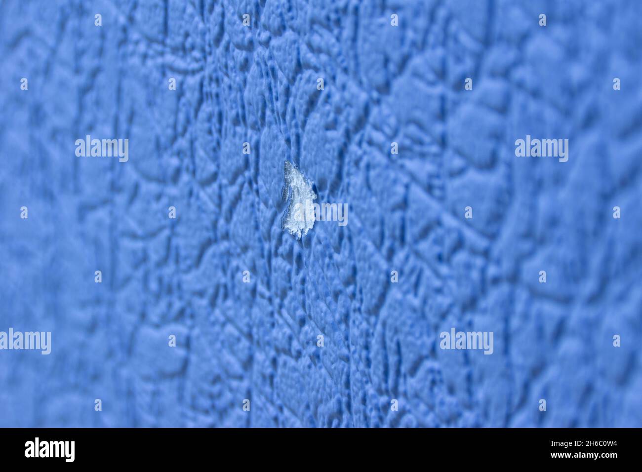 In the new blue wall, damaged vinyl wallpaper damage resulted in a large white spot, selective focus Stock Photo