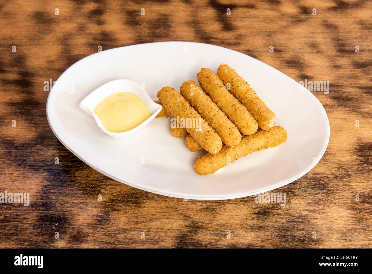 Ration of mozzarella sticks battered and fried in olive oil with mayonnaise sauce for dipping on a white plate Stock Photo