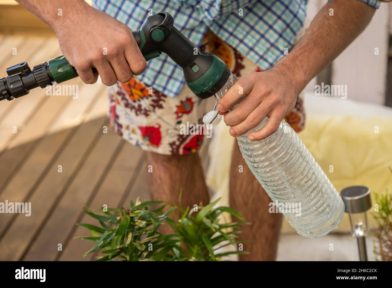 Hombre vestido con una camisa a cuadros llenando una botella de agua para regar las plantas en una terraza urbana Stock Photo