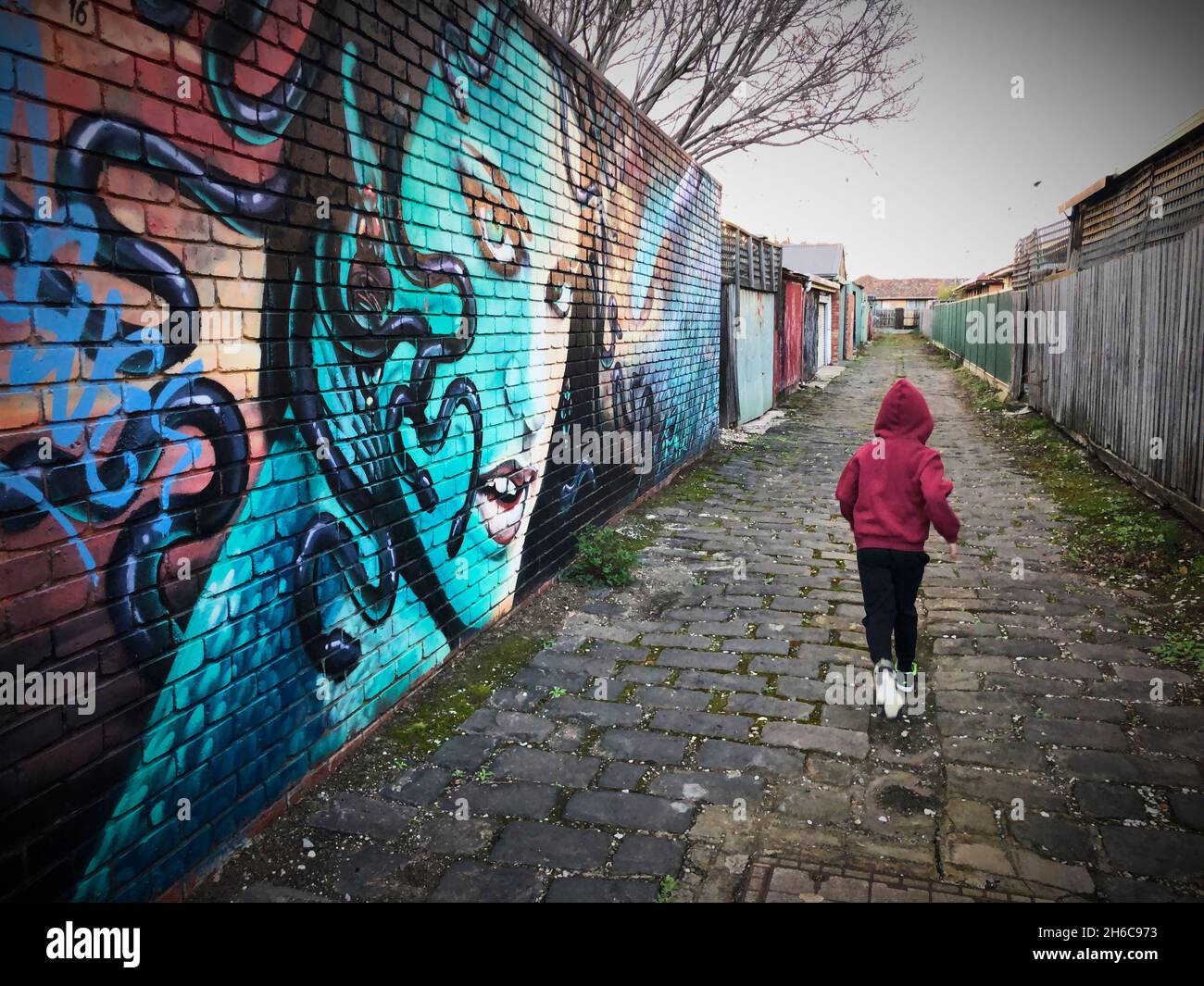 A child in a red hooded jacket runs down a graffitied laneway in West Footscray, Melbourne Australia, August 2021. Stock Photo