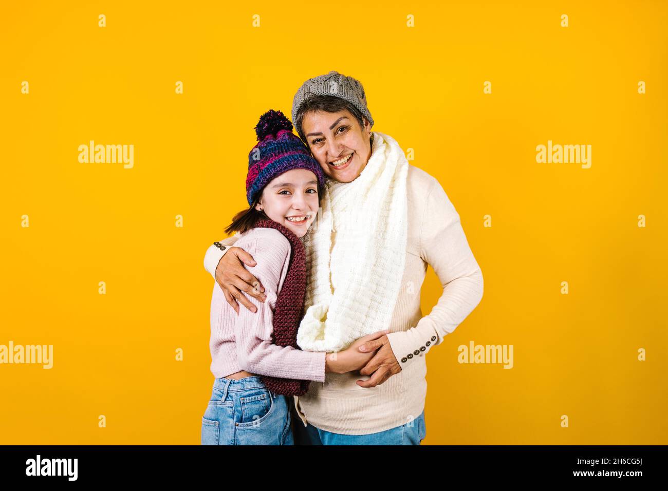 Winter portrait of happy latin family grandmother and granddaughter on yellow background in