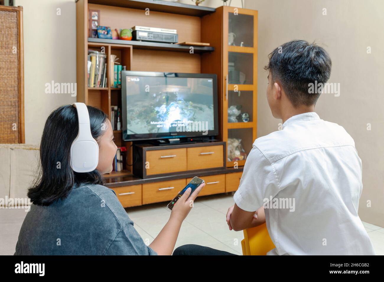 Young Indonesian male watchin tv and sister listening music Stock Photo