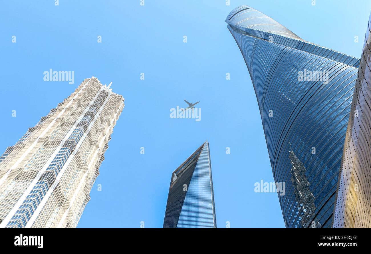 Plane flies above modern skyscrapers in Shanghai in blue sky, Shanghai iconic mega city in China Stock Photo