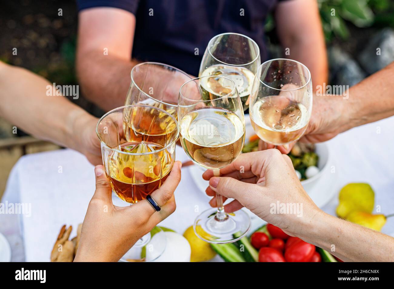 Happy family having dinner at the summer garden party and clinking drinks. People say toast and drink. Festive family dinner in the backyard. Male and Stock Photo