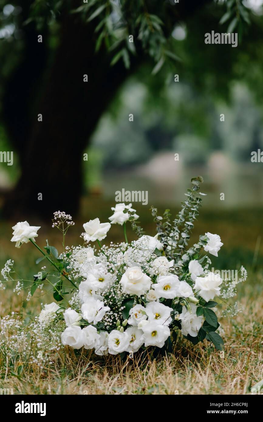 Floral arrangement with white roses and greenery stands against the background of trees Stock Photo