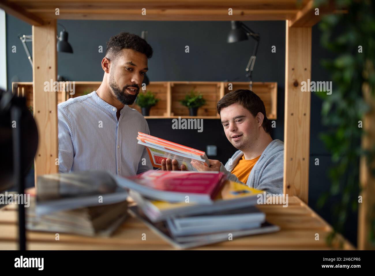 Young happy man with Down syndrome and his tutor indoors at staffroom. Stock Photo