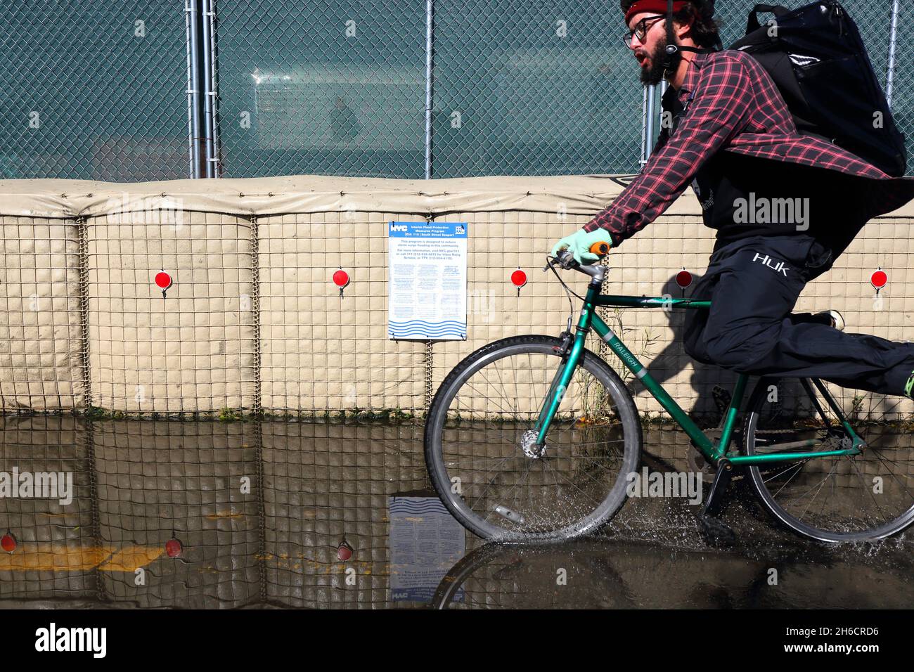 A bicyclist flies by on a flooded section of the East River Greenway flanked by Hesco flood protection barriers. Stock Photo