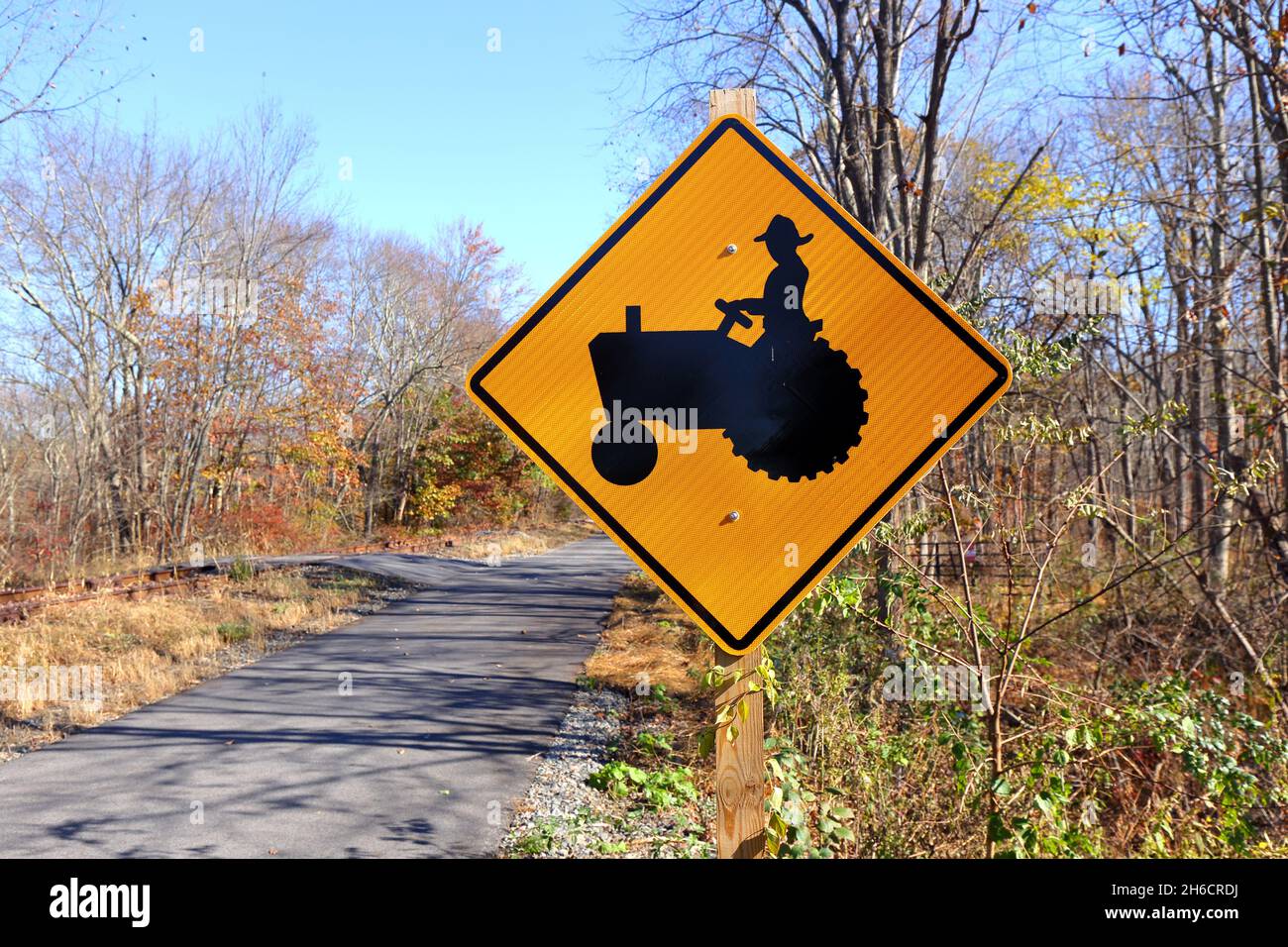 A farm vehicle traffic warning sign on a country road. Farm equipment crossing and farm machinery traffic warning sign. Stock Photo