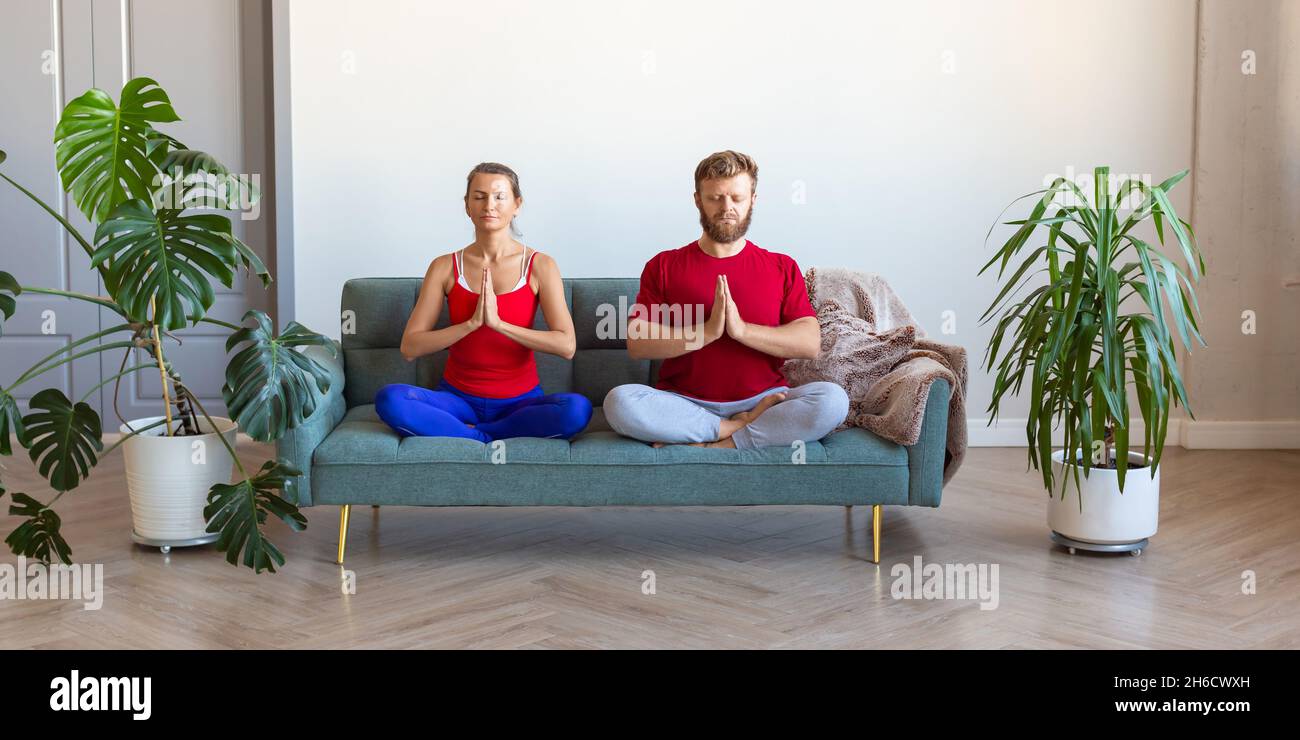 A middle-aged couple is meditating while sitting on the couch. The concept of mental health and a healthy lifestyle. Format photo 2x1. Stock Photo