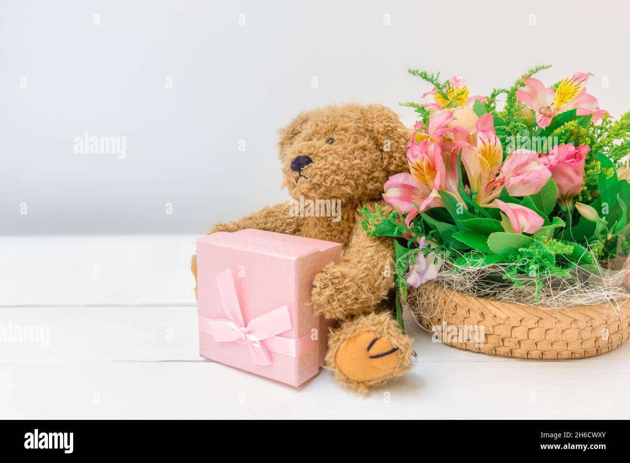 Cute festive background with flowers bouquet, teddy bear and present on white background with copy space Stock Photo