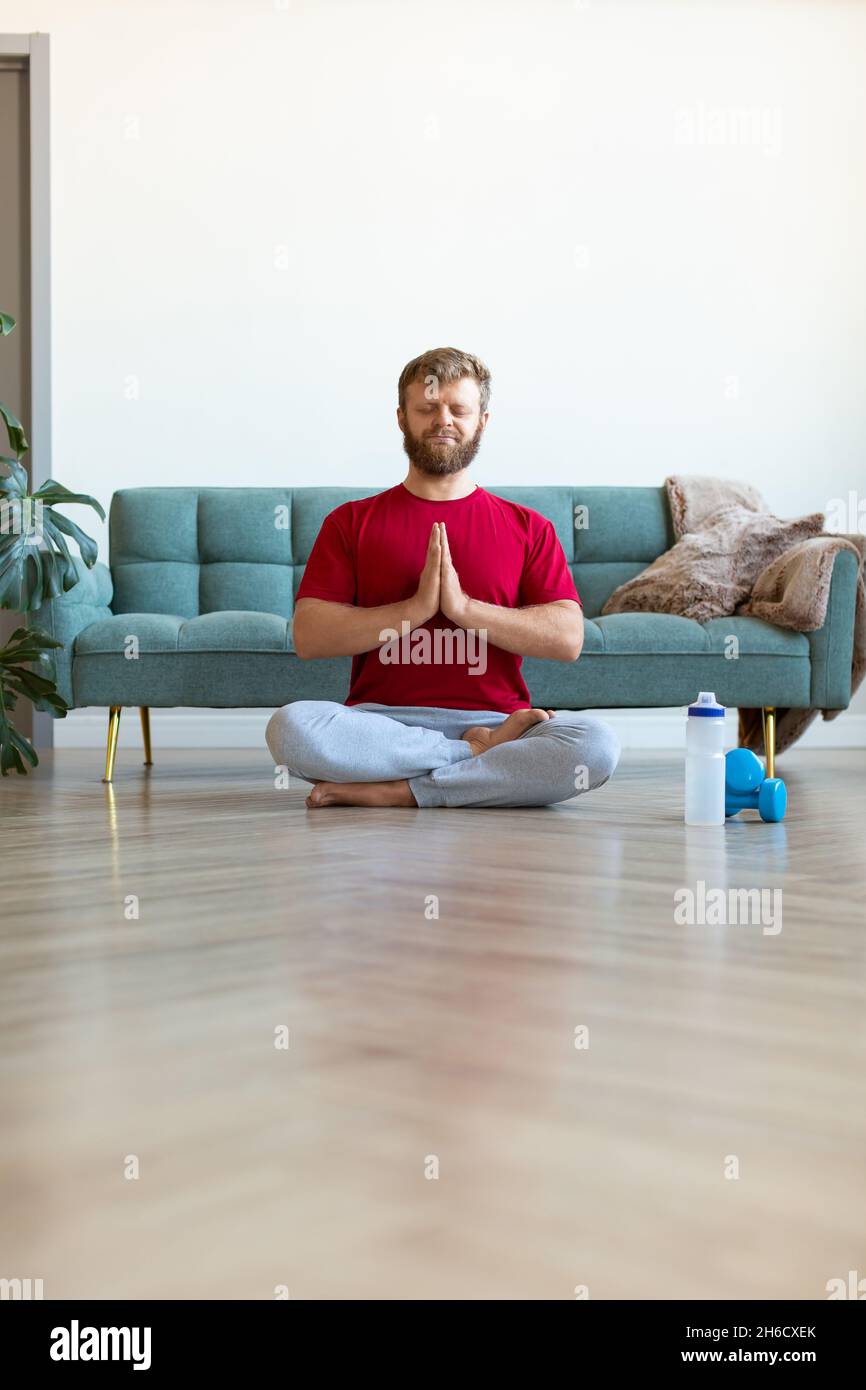 Yoga practice at home - middle aged man meditating while doing yoga. Workout at home. Full-length vertical photo. Stock Photo