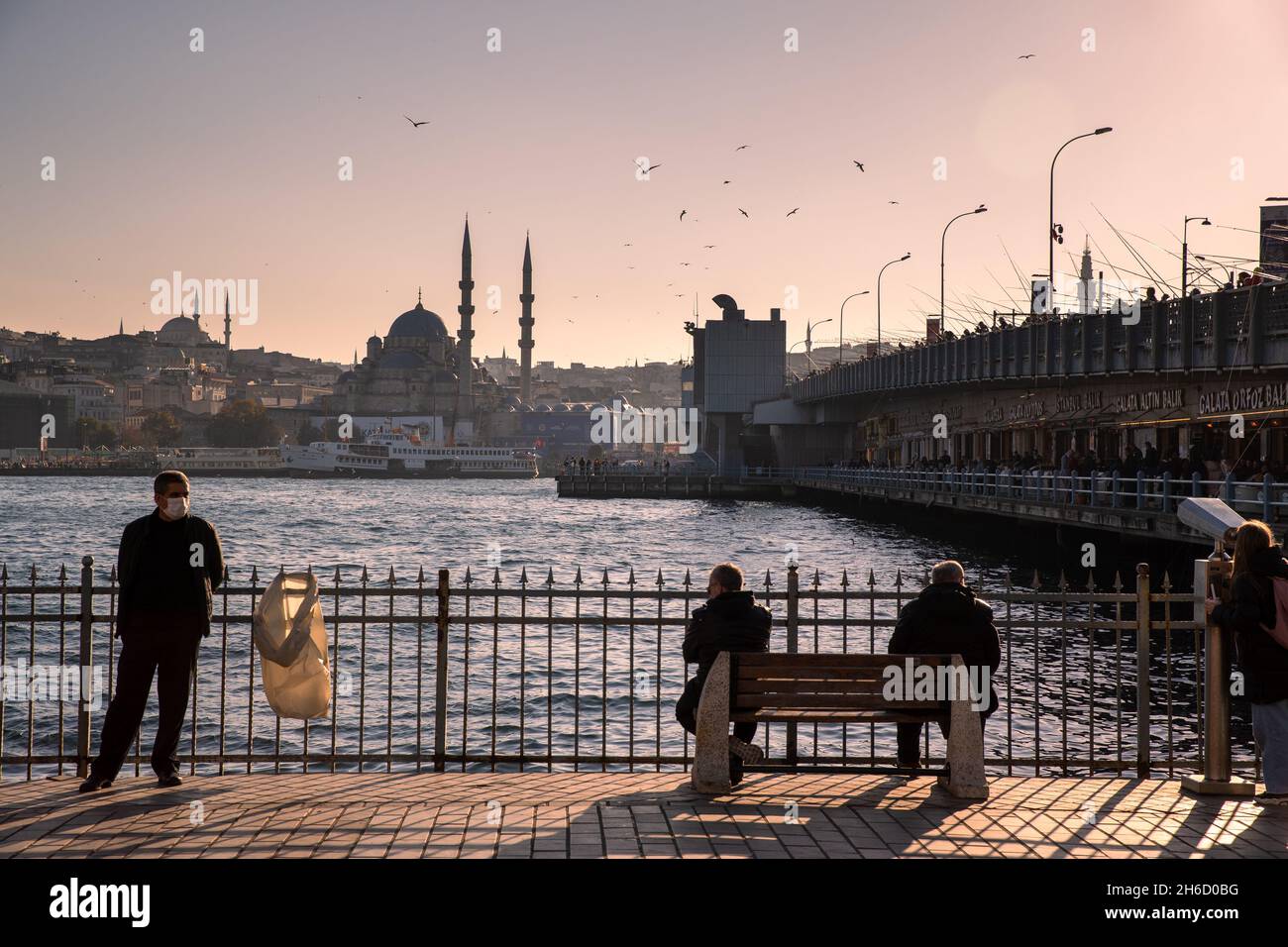 Istanbul, Turkey-Nov.12, 2021: People sit on the benches facing the Golden Horn and the New Mosque and enjoy the beautiful weather in winter. Stock Photo