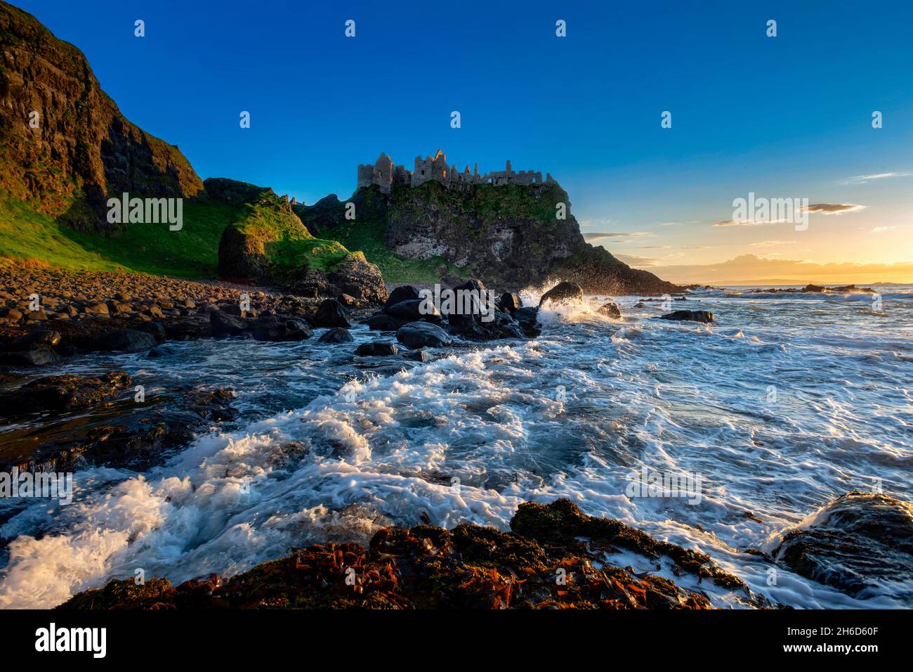 Ruins of Dunluce castle silhouetted by the sun setting off the Irish coast Stock Photo