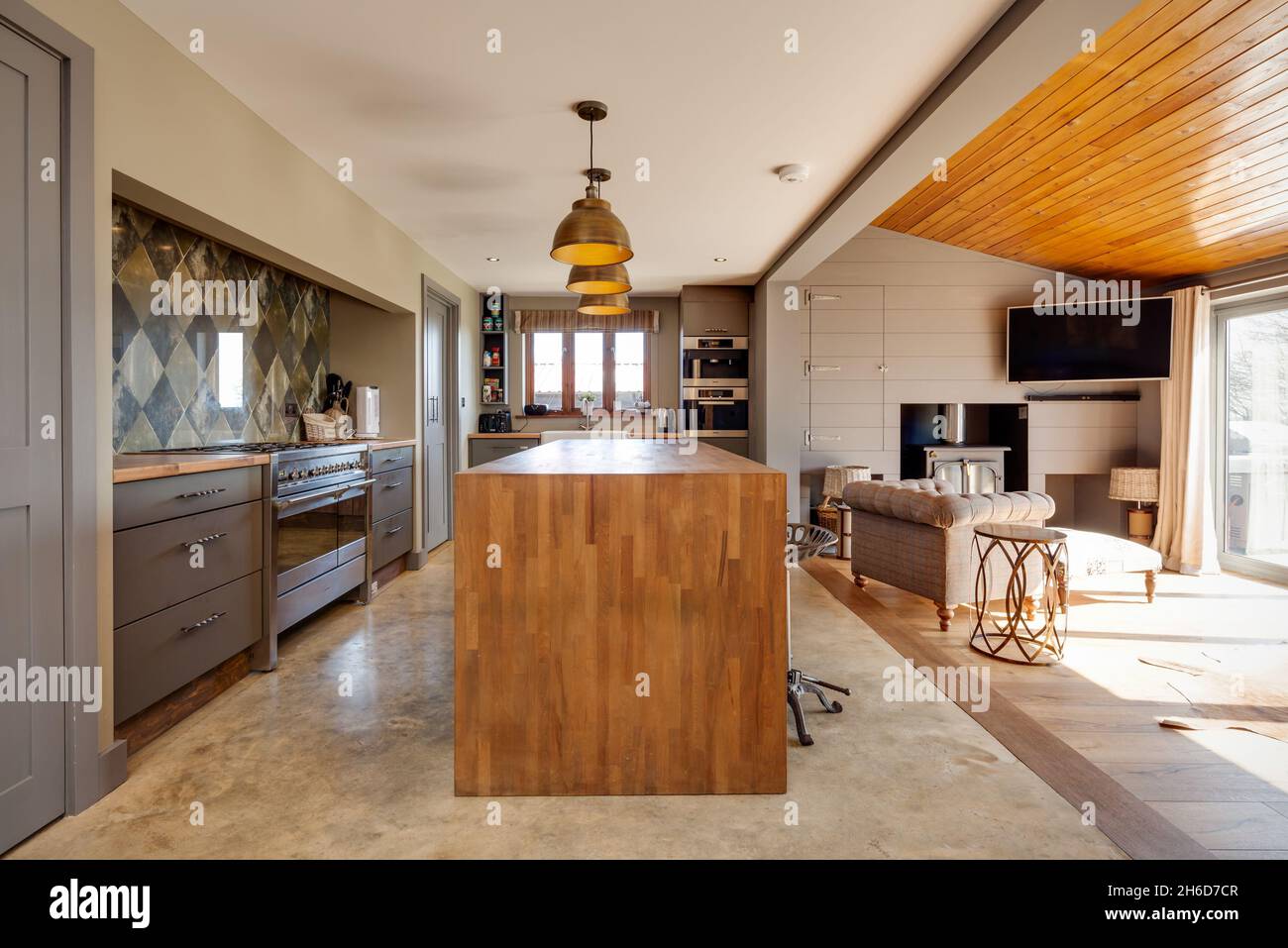 Suffolk, England - March 2018: Home interior kitchen family room showing breakfast bar with stools and seating area in front of wood burning stove. Stock Photo