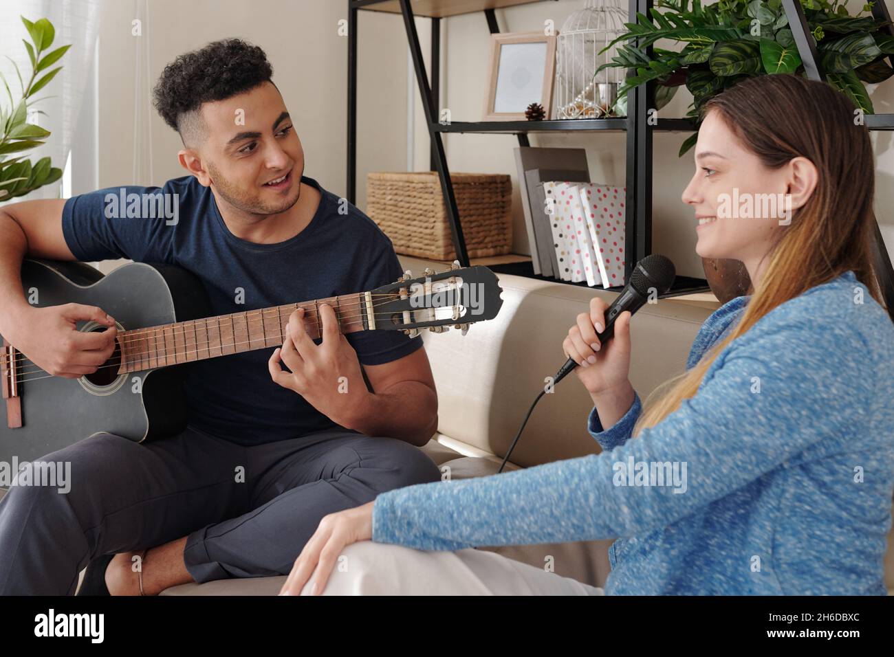 Happy man playing guitar and looking at pretty smiling singing girlfriend Stock Photo
