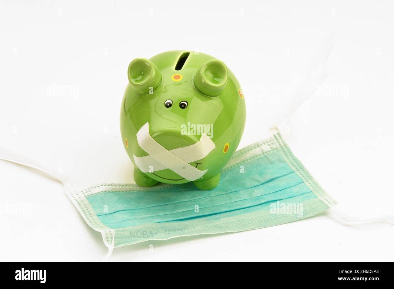 green piggi bank with duct-taped mouth on a surgical mask, coronavirus denier is muzzled Stock Photo