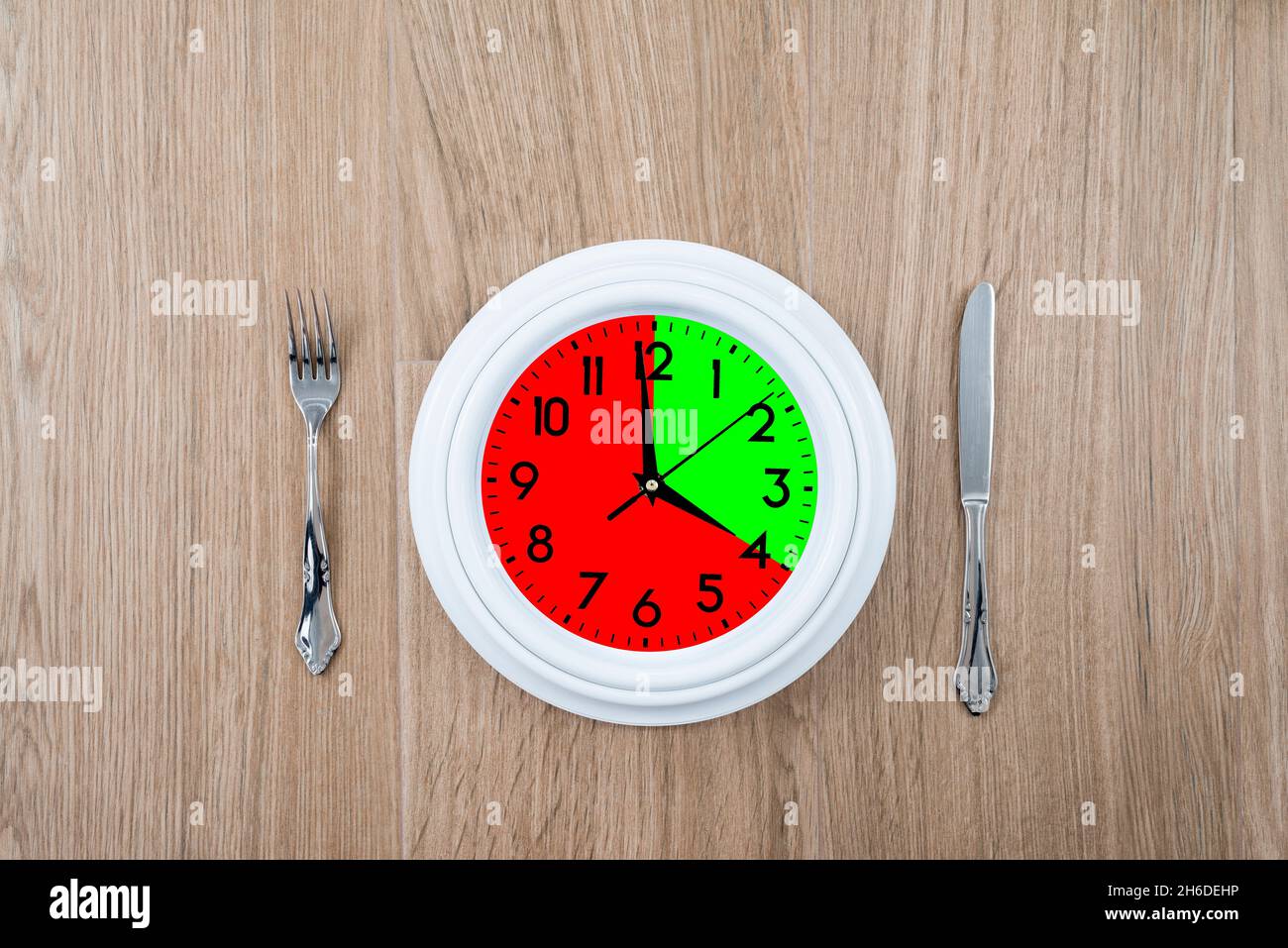 Clock with one portion marked in red and another in green. Concept of intermittent fasting, a diet that provides benefits such as the regenerative mec Stock Photo