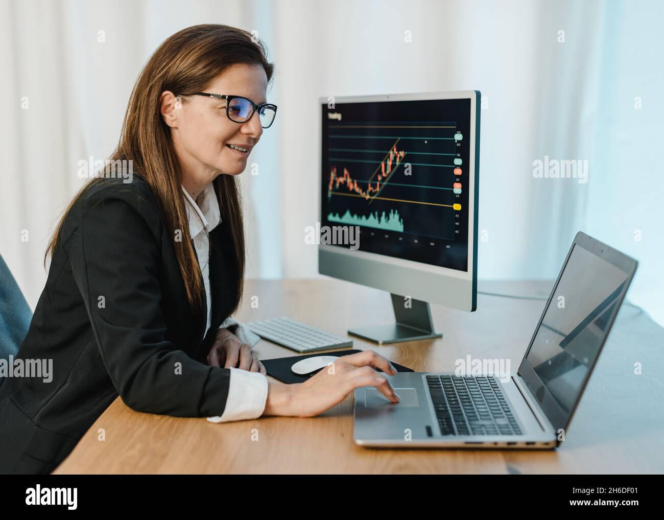 Smiling female trader working on laptop Stock Photo