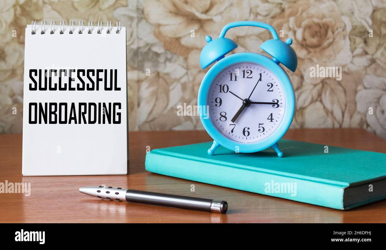 A symbol of successful adaptation. On the notebook the text Successful adaptation. Beautiful background with a diary, a clock and a pen on a wooden ta Stock Photo