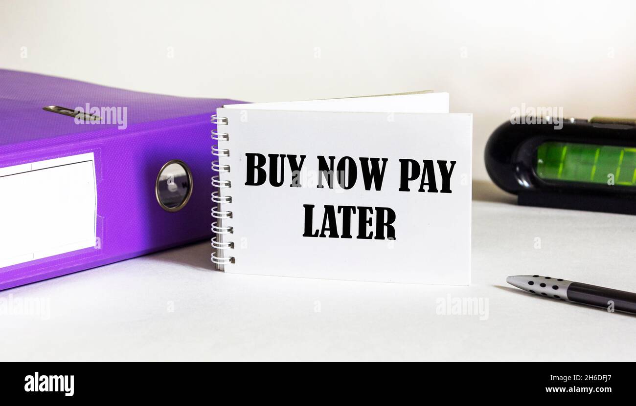 Buy now pay later concept text written on a notebook and a white background, next to a folder with documents, a watch and a pen Stock Photo