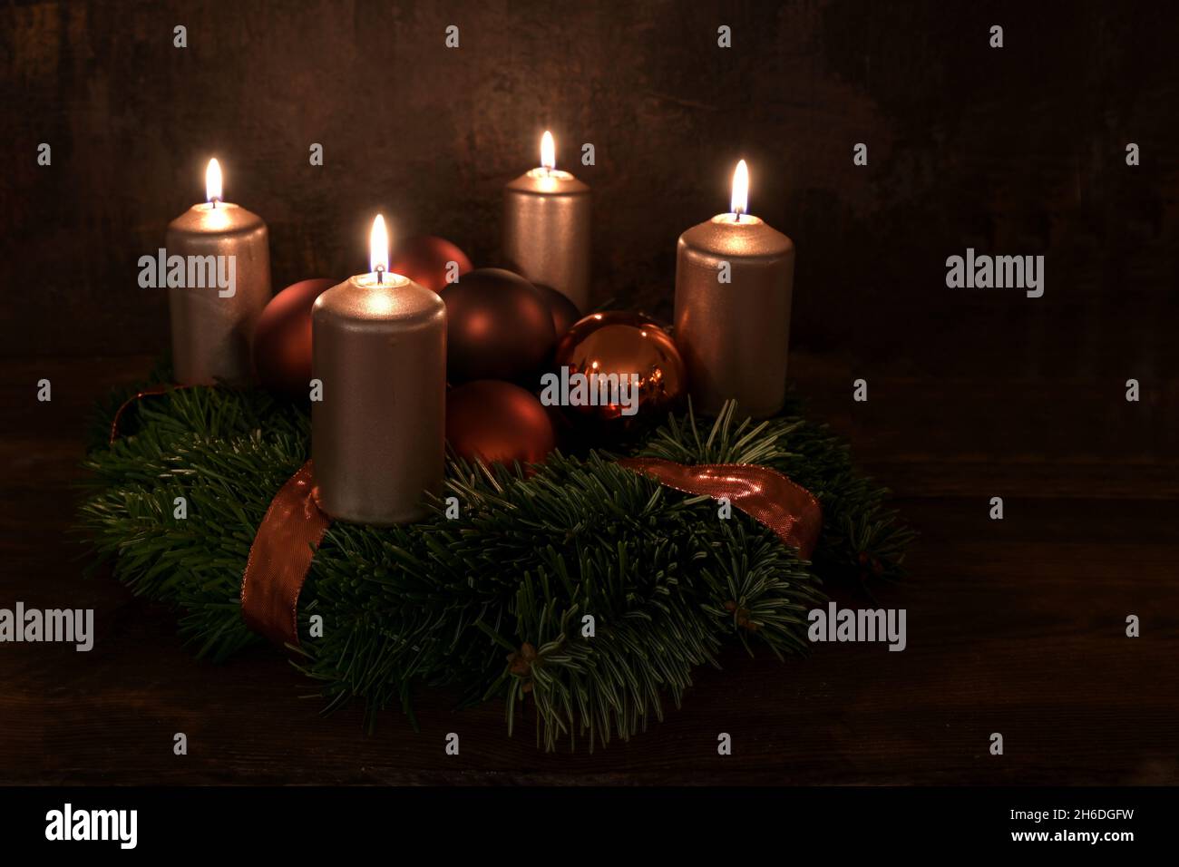 Small Advent wreath with four lit copper colored candles and Christmas decoration baubles against a dark brown rustic background, copy space, selected Stock Photo