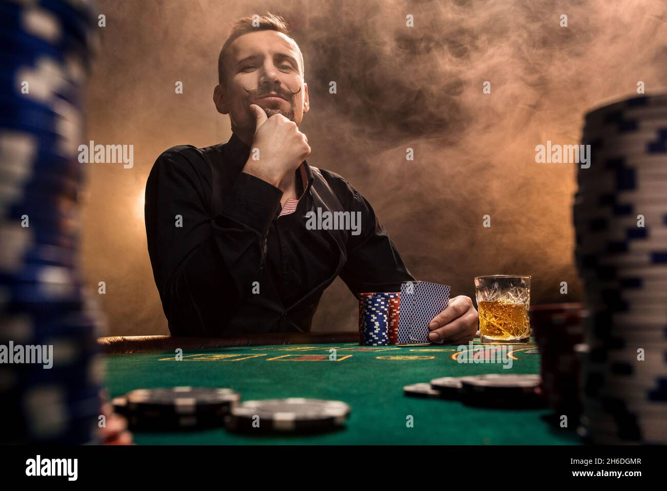 Handsome bearded man drinking whisky while playing poker Stock Photo